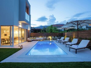 Ein modernes Haus mit Pool, Außenbereich zum Sitzen und einer gut beleuchteten Terrasse.