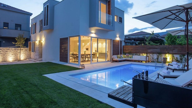 Een modern huis met twee verdiepingen, een zwembad, zitplaatsen buiten en een goed verlicht terras.