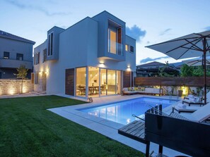 A modern two-story house with a swimming pool, outdoor seating, and a well-lit patio area. - Luxurious Villa With Private Pool and Garden (Kastela)