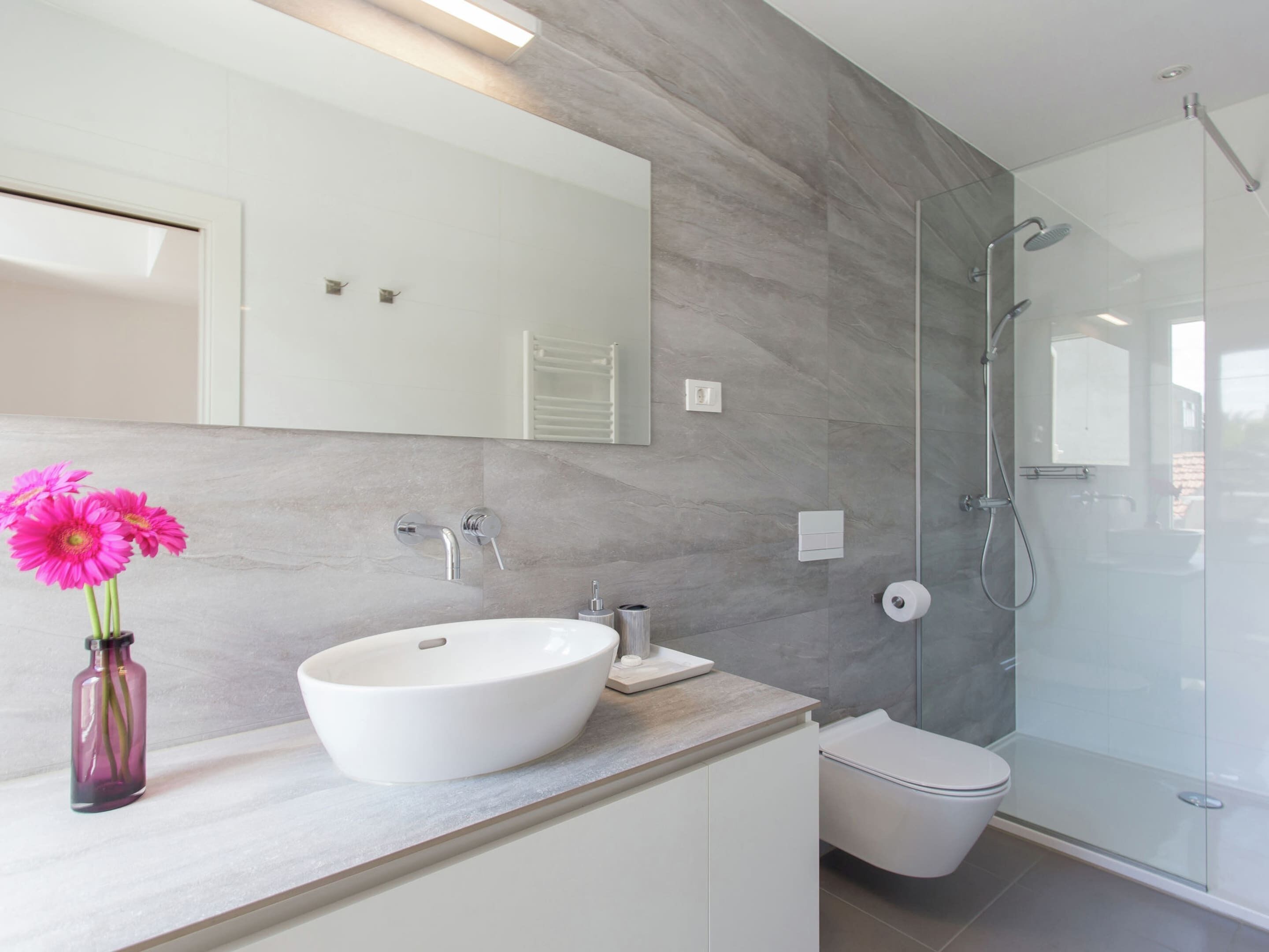 Un baño moderno con un espejo grande, un lavabo blanco, un inodoro y una ducha con mampara de vidrio.