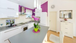 A modern kitchen with white cabinets, a central island with a green bowl of flowers, and a white chair. - Luxurious Villa in Dalmatia Near Sea (Nin)
