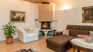 A cozy living room with a fireplace, a white armchair, a brown sofa, and a potted plant.