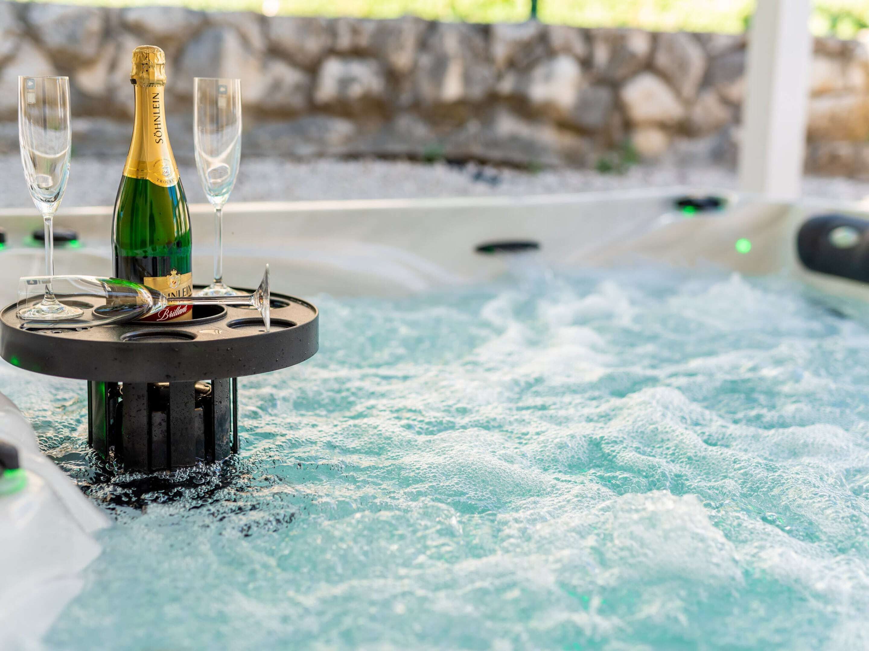 A hot tub with a bottle of champagne and two glasses on a table.