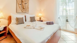 A hotel room with a large bed, two bedside lamps, a painting on the wall, and a view of palm trees through the window.