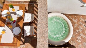 An outdoor dining area with a table set for two, a hot tub, and a tiled floor.