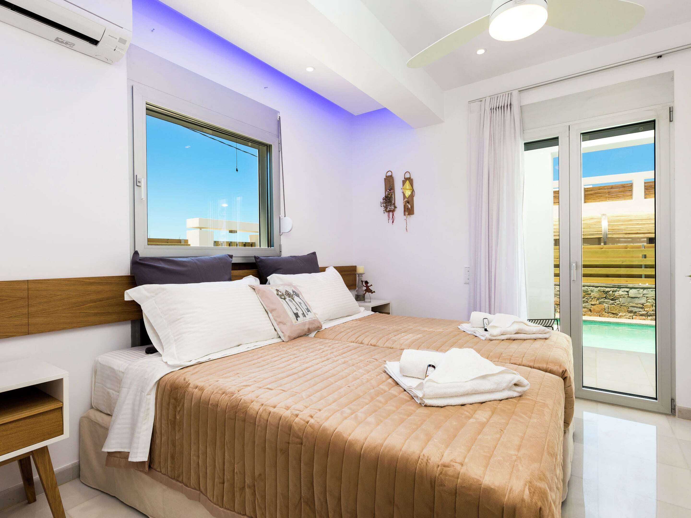 A modern hotel room with a large bed, a bedside table, a window with a view, and a sliding glass door to the balcony.