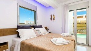 A modern hotel room with a large bed, a bedside table, a window with a view, and a sliding glass door to the balcony. - Luxury Villa, Private Pool & Beach, Pigianos Kampos, Rethymno Area, NW Coast (Rethymno)