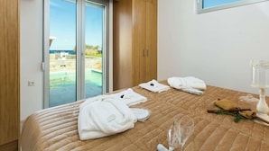 A hotel room with a bed, a glass of water, towels, and a view of a pool and ocean. - Luxury Villa, Private Pool & Beach, Pigianos Kampos, Rethymno Area, NW Coast (Rethymno)