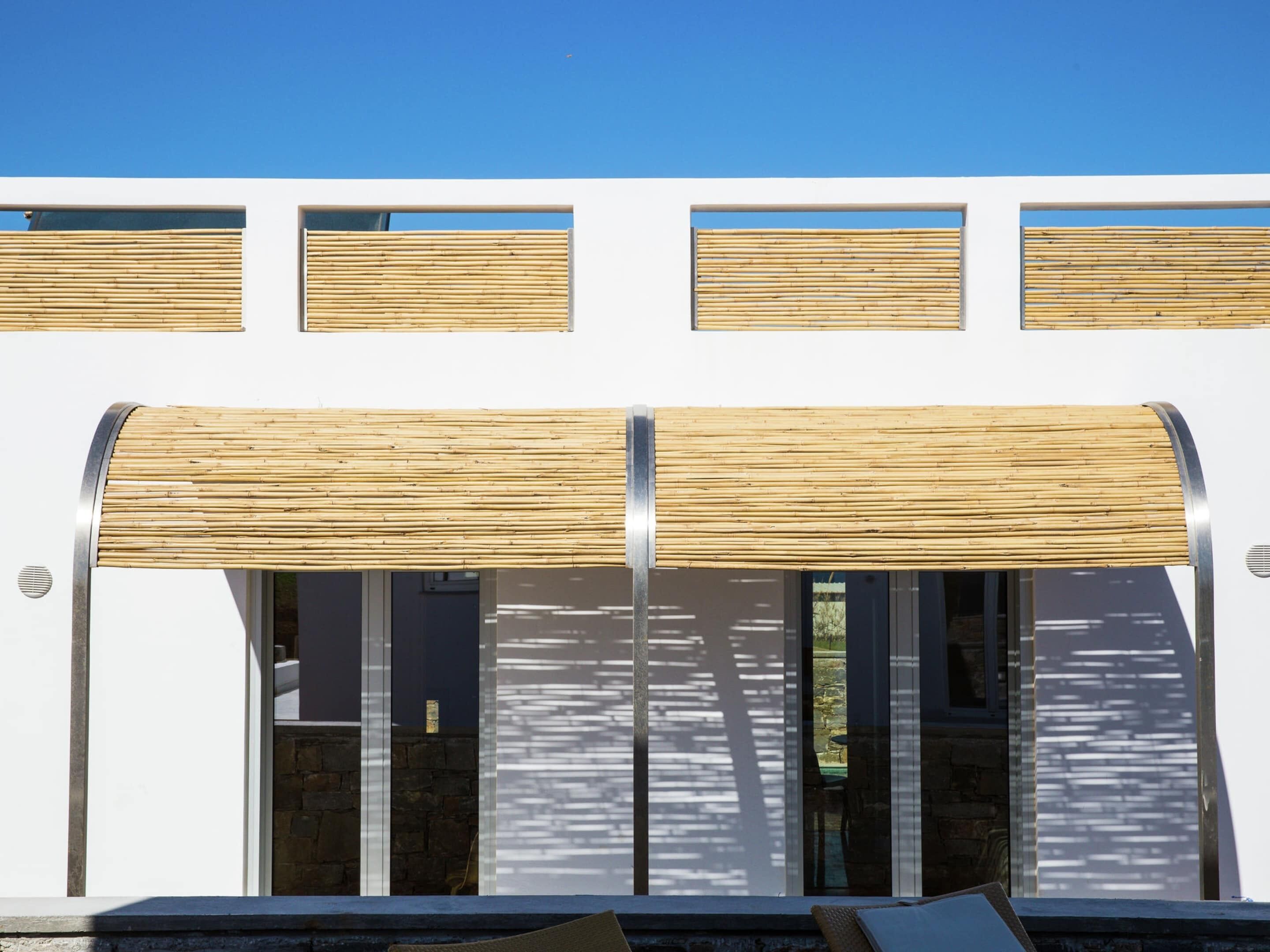 Un bâtiment moderne à la façade blanche, doté de grandes fenêtres et d’un auvent en bambou au-dessus de l’entrée.