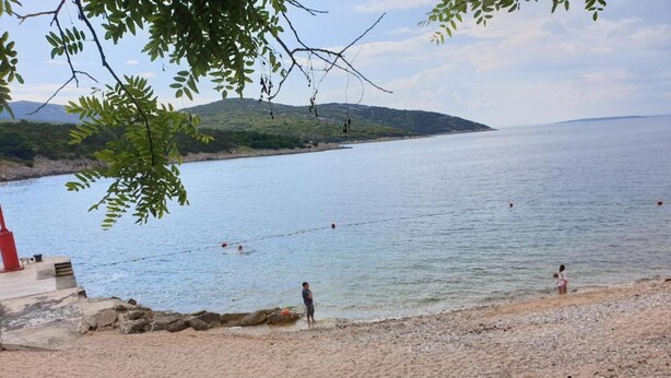A beach with a rocky shoreline, a few people swimming, and a distant hill. - Holiday Home in Osor Near Sandy Beach (Mali Losinj)