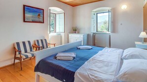 A bedroom with a wooden ceiling, a bed with white and blue bedding, a chair, a desk, and a window with a view of the outdoors. - Holiday Home in Osor Near Sandy Beach (Mali Losinj)