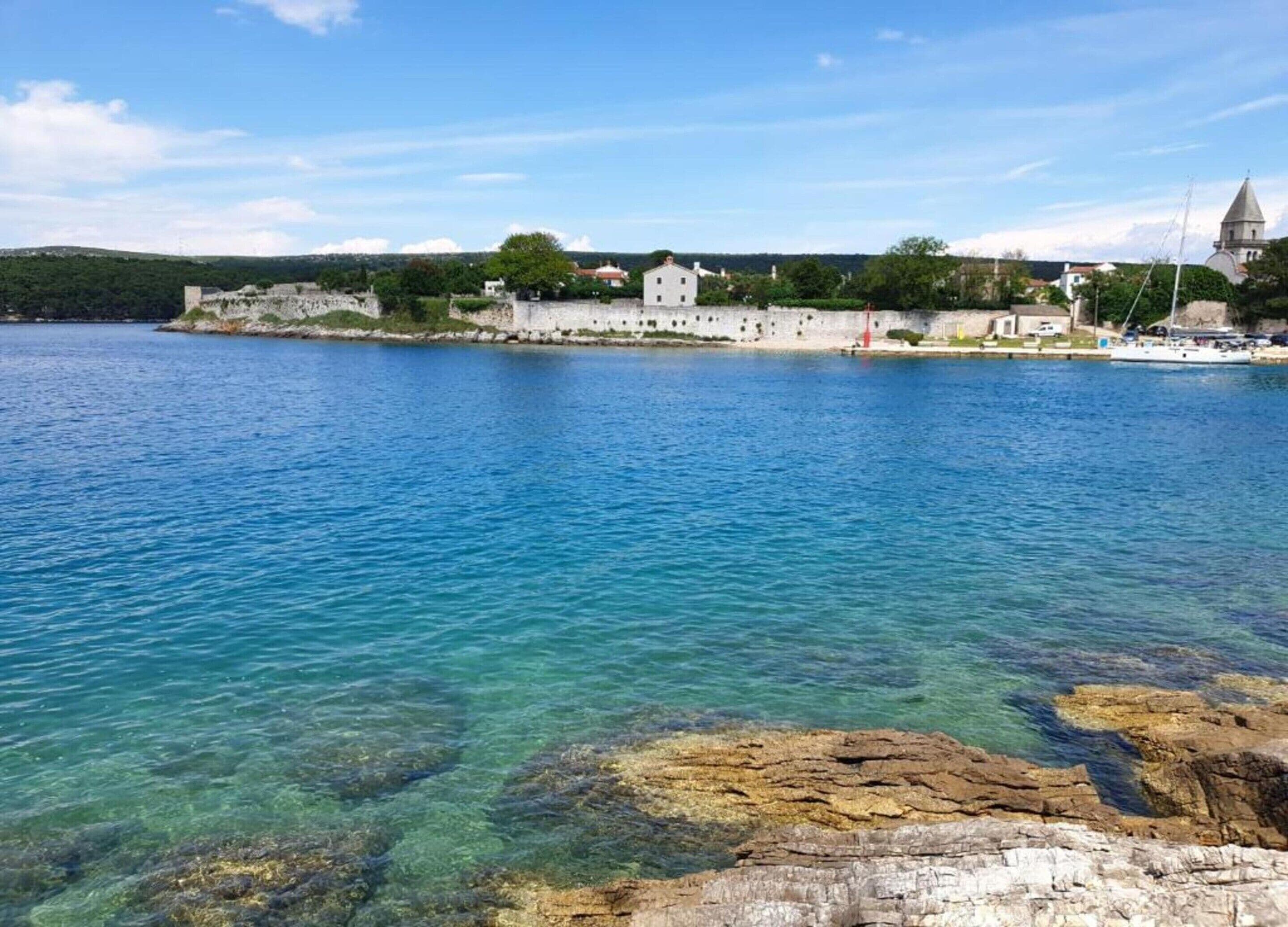 Une vue sur la côte, avec une eau d’un bleu limpide, un rivage rocheux et un bâtiment historique doté d’une tour.
