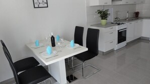 Een moderne keuken met witte kastjes, een gasfornuis en een spoelbak. Er staat een eettafel met stoelen en een potplant op het aanrecht.