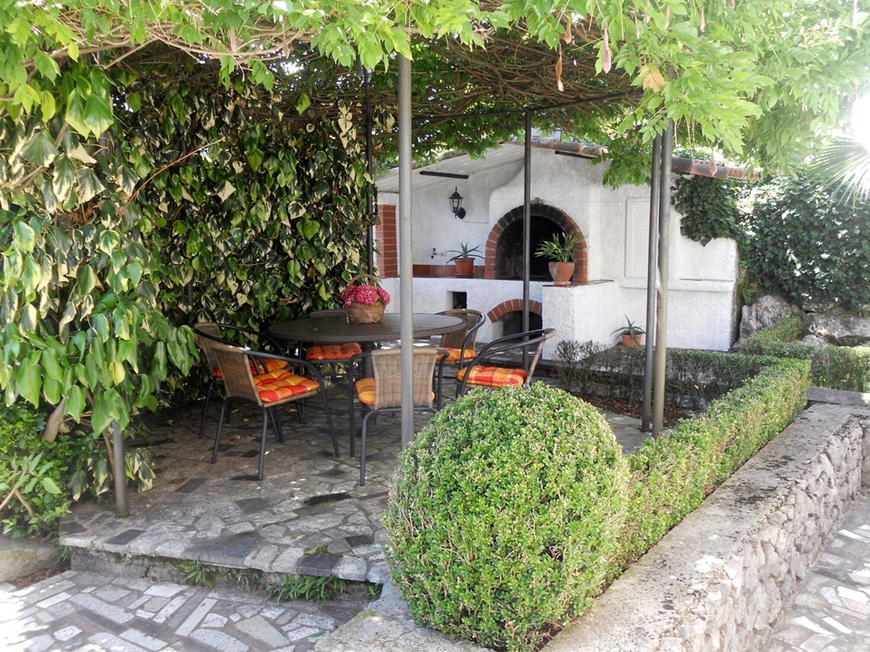 An outdoor patio with stone flooring, a round table, and chairs with orange cushions.