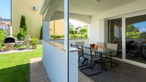 A patio with a table and chairs, a barbecue grill, and a glass door leading to a garden. - Modern Apartment With Roof Terrace Near the Beach (Malinska-Dubasnica)