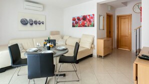 A modern living room with a sofa, a dining table with chairs, a coffee table, and a painting on the wall. - Modern Apartment With Roof Terrace Near the Beach (Malinska-Dubasnica)