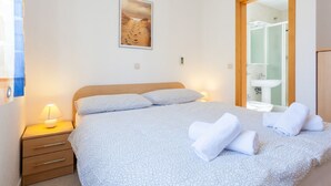A bedroom with a bed, a nightstand, a lamp, a framed picture on the wall, and a bathroom visible through an open door. - Modern Apartment With Roof Terrace Near the Beach (Malinska-Dubasnica)