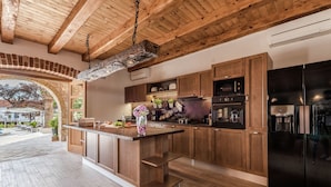 A modern kitchen with wooden cabinets, a black refrigerator, and a stone archway leading to an outdoor patio. - Villa in Sukosan With Pool Near the Sea (Sukosan)