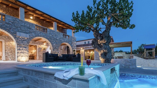 A stone building with a swimming pool, outdoor seating, and a tree. - Villa in Sukosan With Pool Near the Sea (Sukosan)