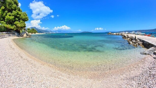 Una spiaggia limpida con un litorale roccioso, una spiaggia di ciottoli e un cielo azzurro intenso.