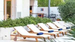 Un'area relax esterna moderna con lettini prendisole, un barbecue e un tavolo da pranzo con sedie.