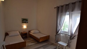 A small, well-lit bedroom with two single beds, a nightstand, a chair, and a window with curtains. - Comfortable Apartment With Balcony and Outdoor Kitchen (Pag)