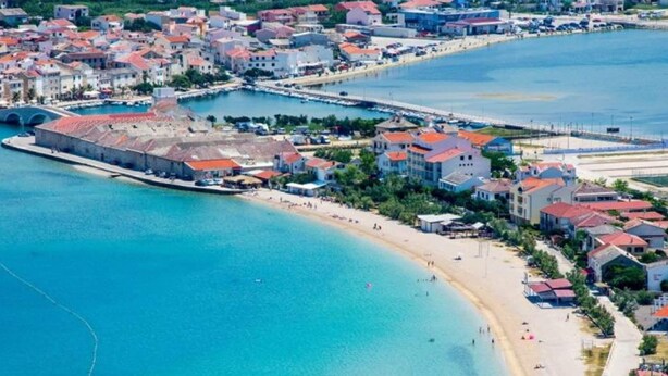 A coastal town with a beach, buildings, and a marina. - Comfortable Apartment With Balcony and Outdoor Kitchen (Pag)