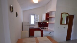 A compact kitchen with a refrigerator, sink, and a dining area with a table and chairs. - Comfortable Apartment With Balcony and Outdoor Kitchen (Pag)