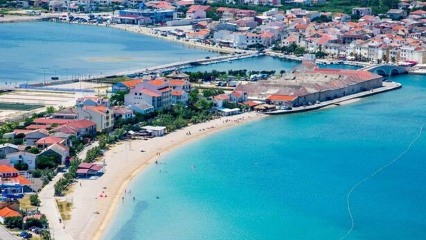Vue aérienne d’une ville côtière avec une plage, des bâtiments et un port.