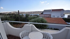 Un balcon avec des chaises blanches et une petite table, donnant sur un quartier résidentiel avec des maisons et une étendue d’eau.