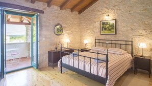 Een slaapkamer met een stenen muur, een houten vloer, een bed met metalen frame, twee nachtkastjes met lampen en een schilderij aan de wand.