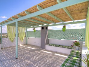 A covered outdoor seating area with a wooden ceiling, green cushions, and potted plants. - Holiday Home in Crete With Private Pool (Rethymno)