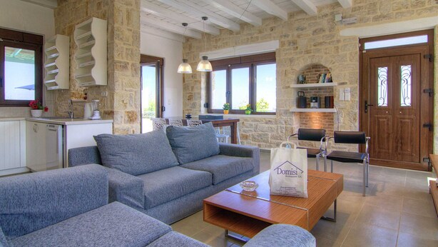 A spacious living area with a stone wall, a sofa, a coffee table, and a kitchen area with a sink and a blender. - Holiday Home in Crete With Private Pool (Rethymno)