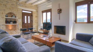 A living room with a stone wall, fireplace, television, and seating area. - Holiday Home in Crete With Private Pool (Rethymno)