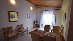Une pièce avec un plafond en bois, une table à manger avec des chaises, un téléviseur posé sur un meuble et une porte-fenêtre coulissante donnant sur un espace extérieur.