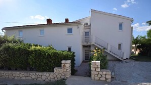 Un immeuble de deux étages avec une façade en pierre, un petit balcon et un escalier menant à l’étage supérieur.