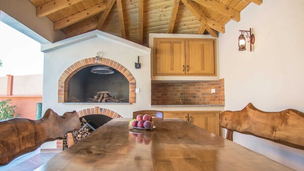 A rustic dining area with a long wooden table, two brick ovens, wooden cabinets, and a hanging lantern. - Holiday Home in Imotski With Pool (Imotski)