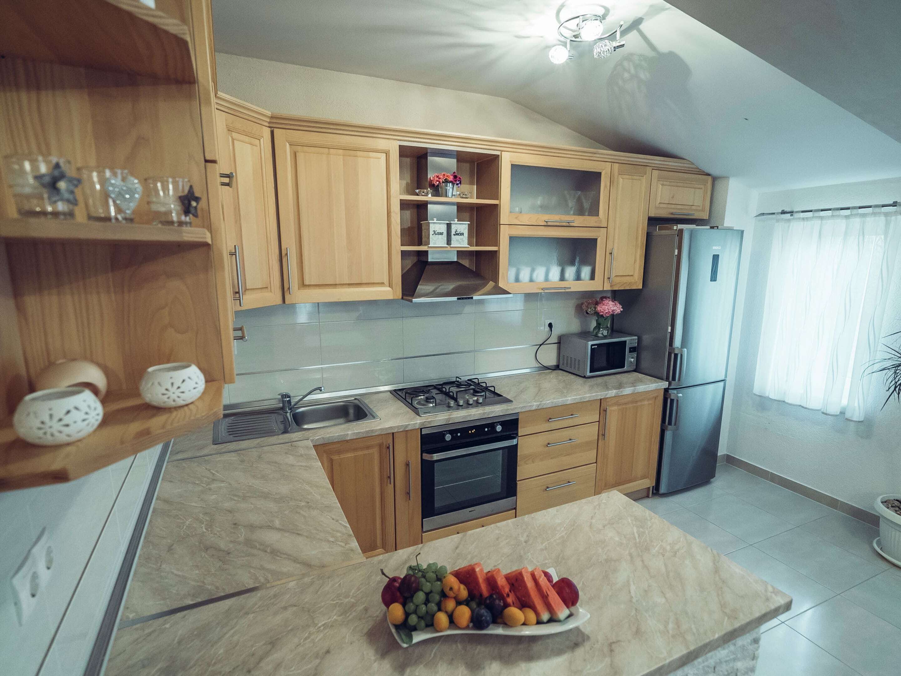Eine moderne Küche mit Holzschränken, einem Edelstahlkühlschrank, einer Mikrowelle und einem Spülbecken.