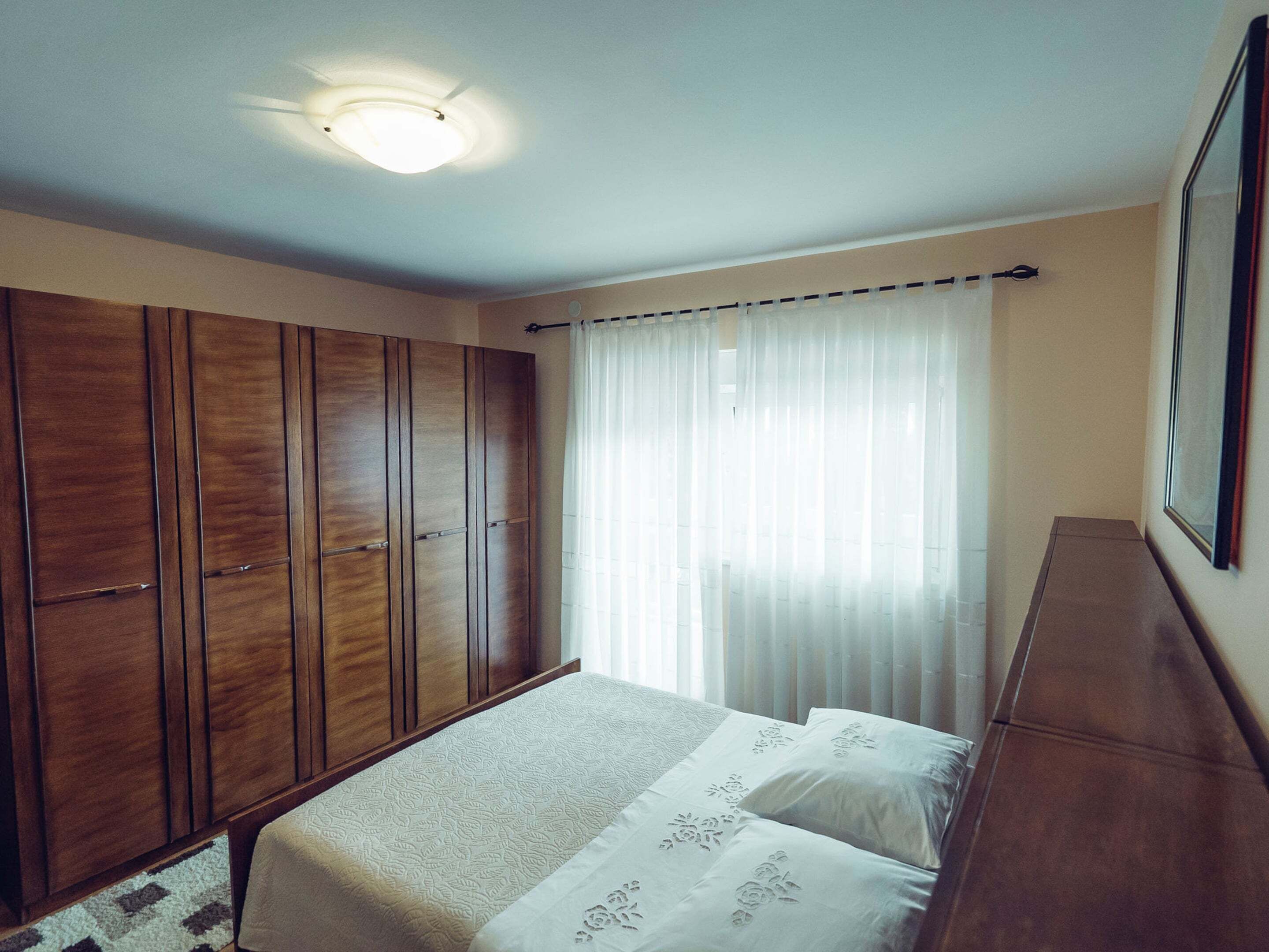 A bedroom with a bed, wooden wardrobe, and a ceiling light.
