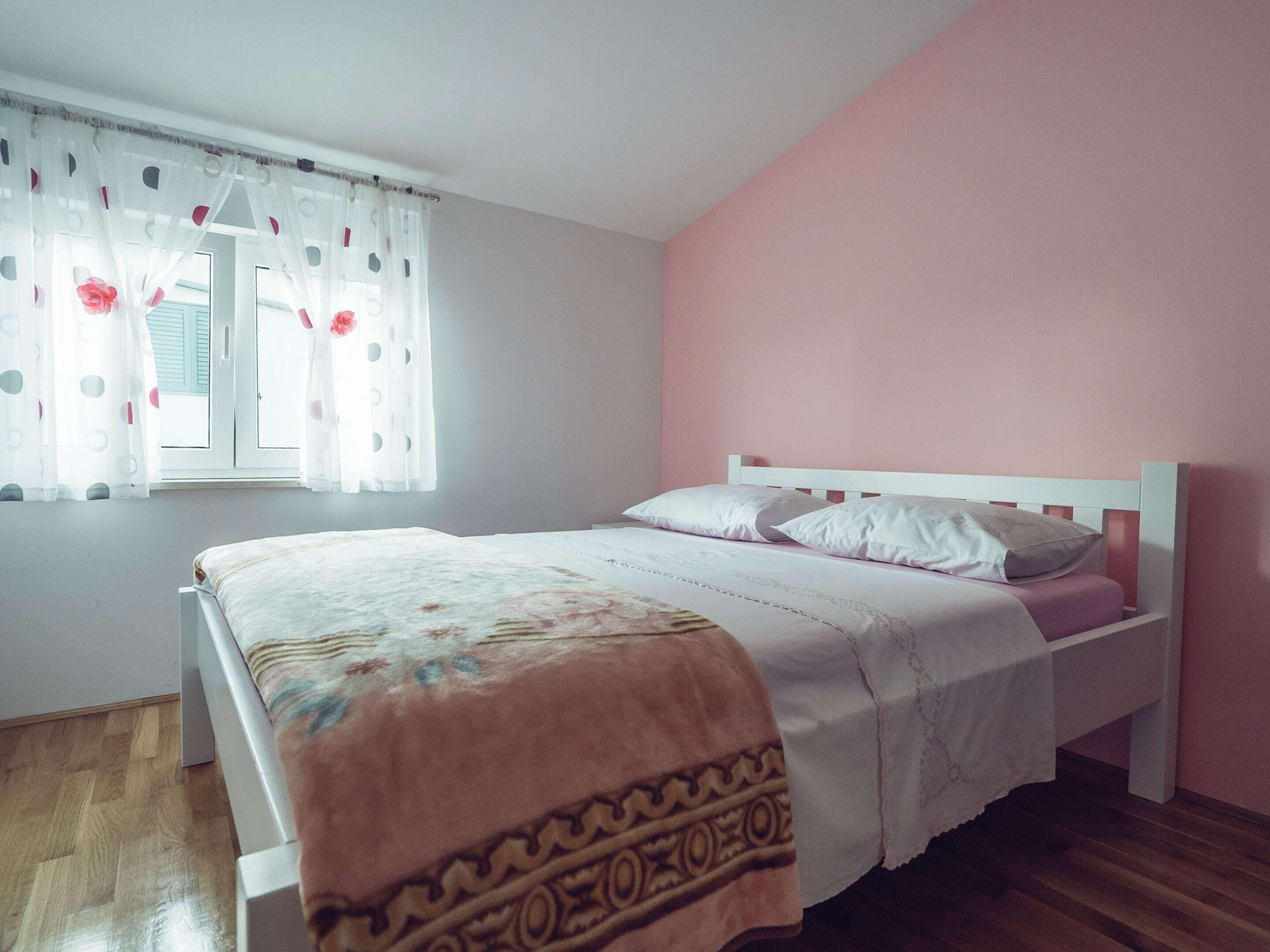 Ein Schlafzimmer mit einem Bett, einem Fenster mit Vorhängen und einer rosafarbenen Wand.