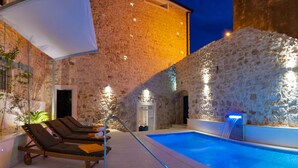 Piscina con sillas de descanso y un muro de piedra.