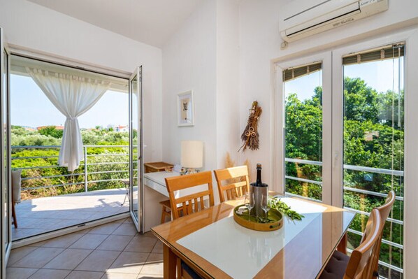 A dining area with a table, chairs, and a view of greenery through large windows.
