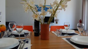 Tavola imbandita per quattro persone, con piatti bianchi, posate e bicchieri, un vaso con fiori bianchi e una bottiglia d'acqua.