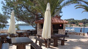 Tavoli e panche all'aperto, un edificio in pietra con tetto in tegole e vista sul mare.