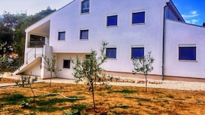 A modern two-story building with a flat roof, multiple windows with shutters, and a small staircase leading to an upper floor.