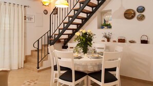 A dining area with a round table set for four, surrounded by white chairs with black cushions. A staircase with wooden steps and black railings leads to an upper level. - Modern Villa in Grohote With Pool (Solta)