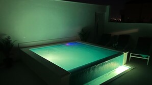 A rectangular swimming pool with a tiled edge, surrounded by a low wall and a few lounge chairs.