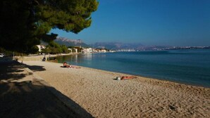 A beach with people sunbathing, a clear sky, and a distant cityscape.