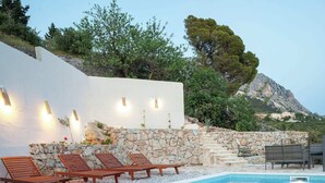 A pool area with stone walls, wooden loungers, and a view of a mountainous landscape. - Villa in Podgora With Pool Near Beach (Podgora)