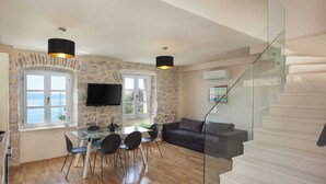 A modern living room with a stone wall, a glass dining table, and a staircase. - Villa in Podgora With Pool Near Beach (Podgora)